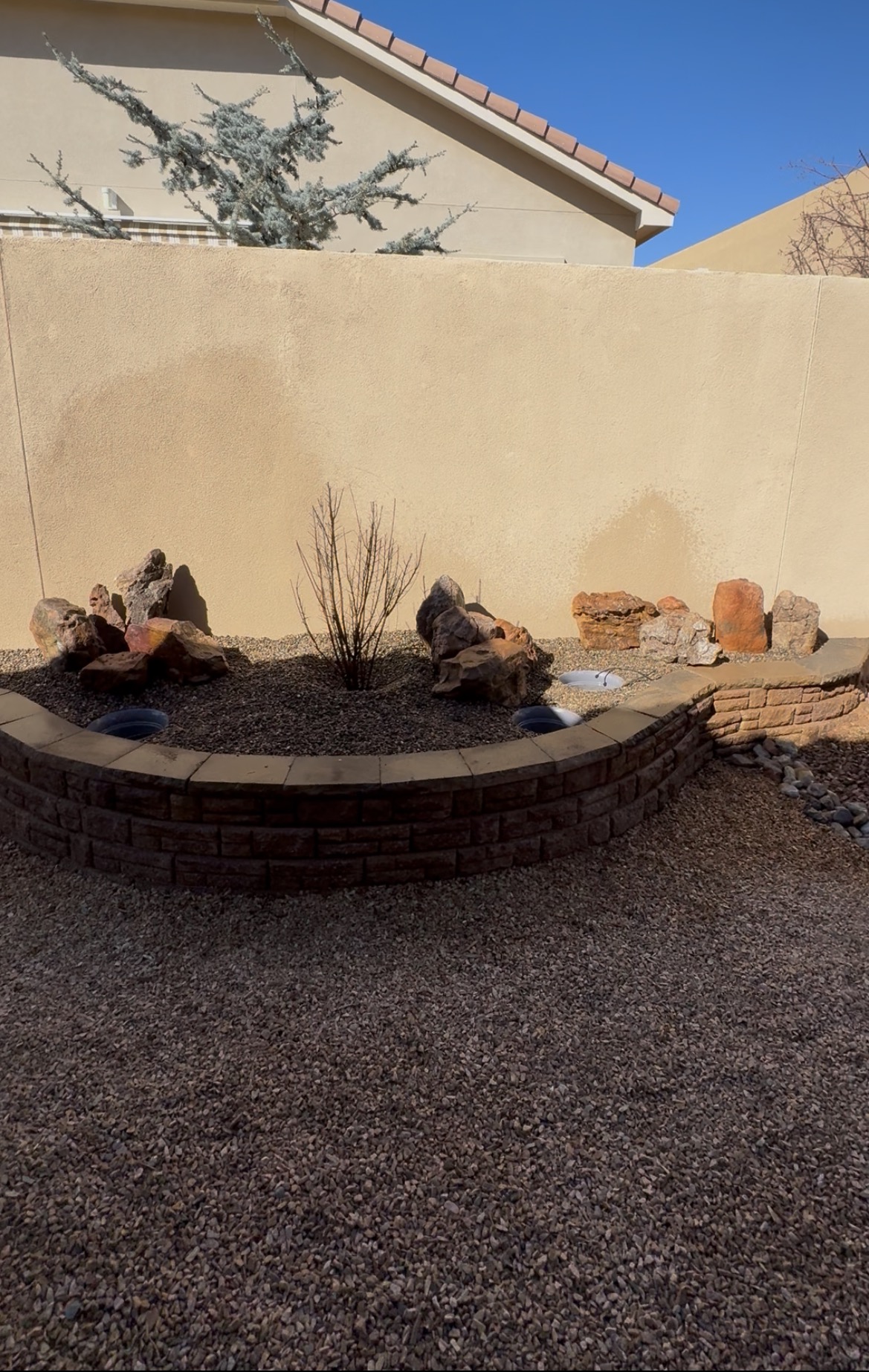 Curved stone retaining wall forming a raised planter bed with boulders and gravel